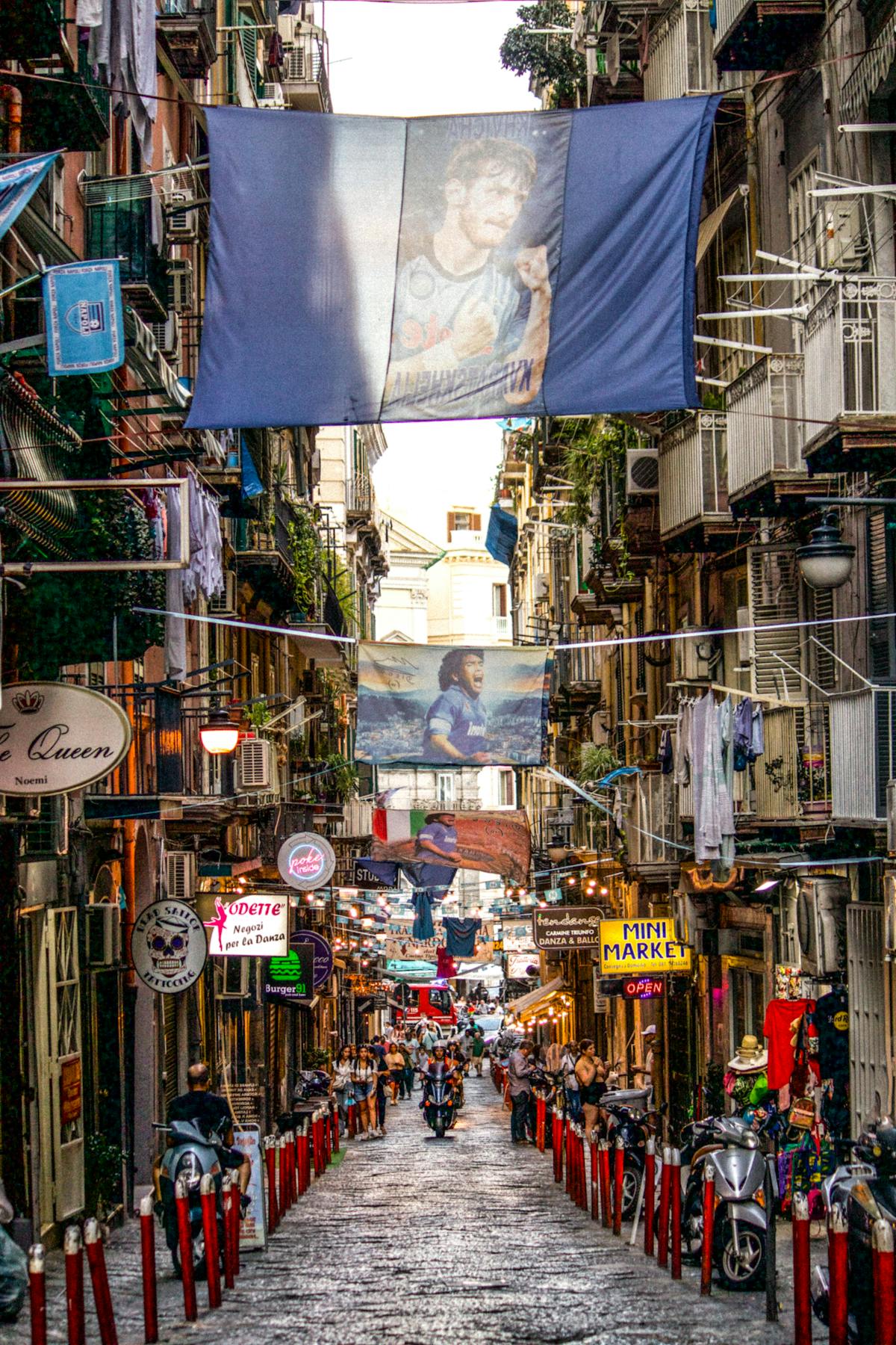 Looking down Spaccanapoli toward the centro storico, laundry hanging between buildings, scooters parked along the narrow street